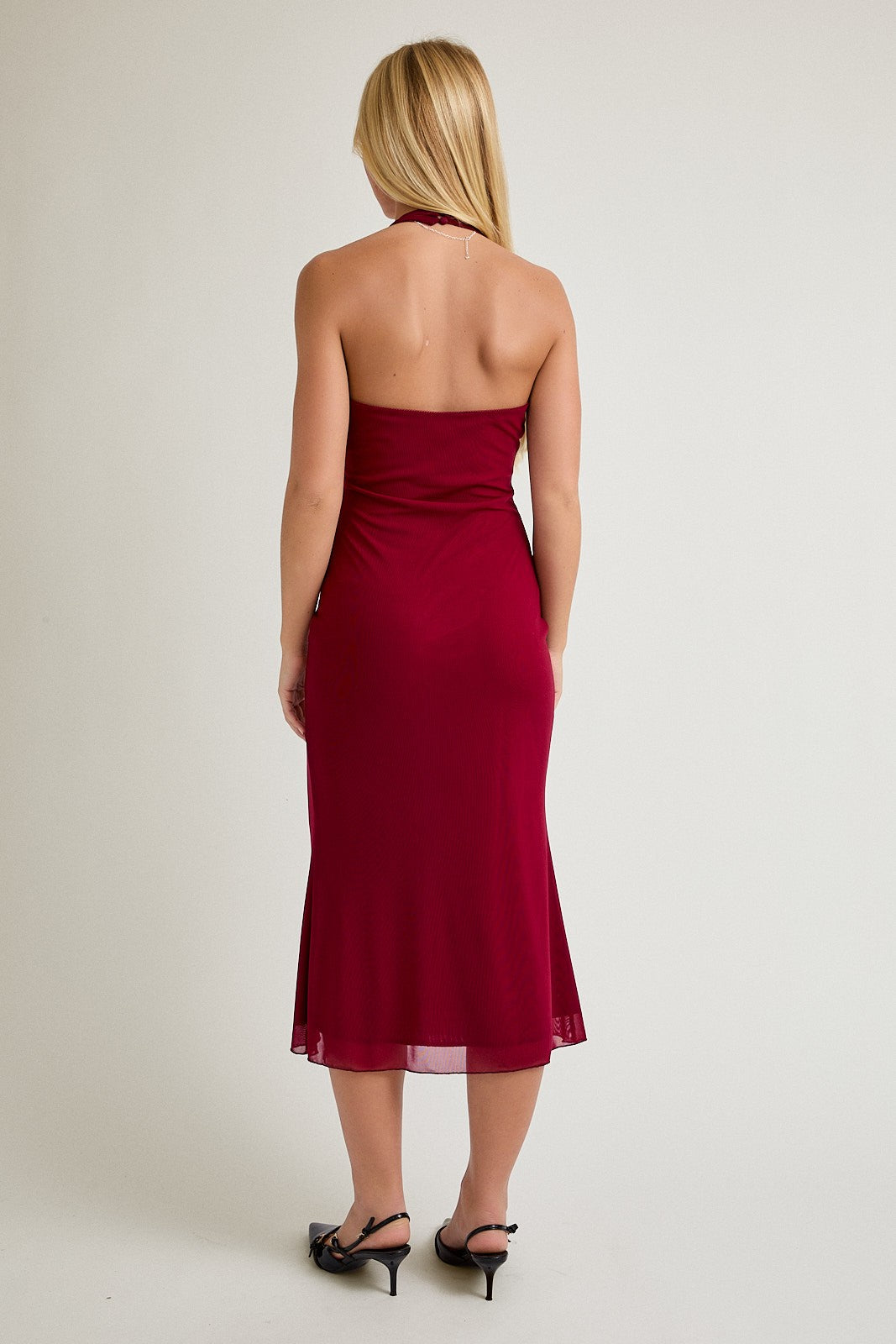 woman wearing a burgundy halter neck midi dress, showing a fitted silhouette from the back