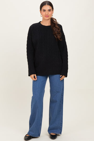 woman wearing a black cable knit sweater and wide leg jeans, standing against a neutral background