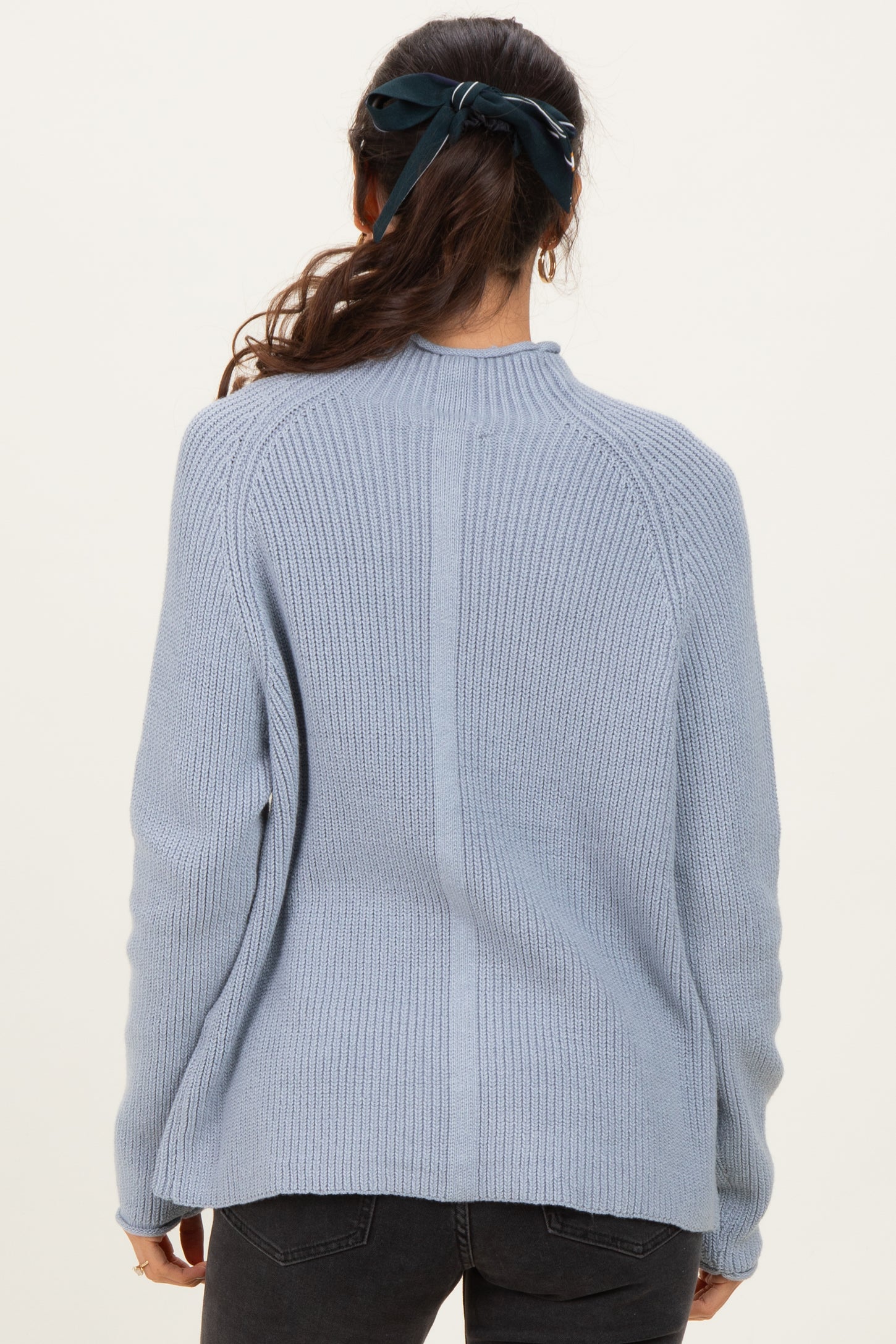 woman wearing a light blue ribbed sweater with a high neckline and long sleeves, viewed from the back