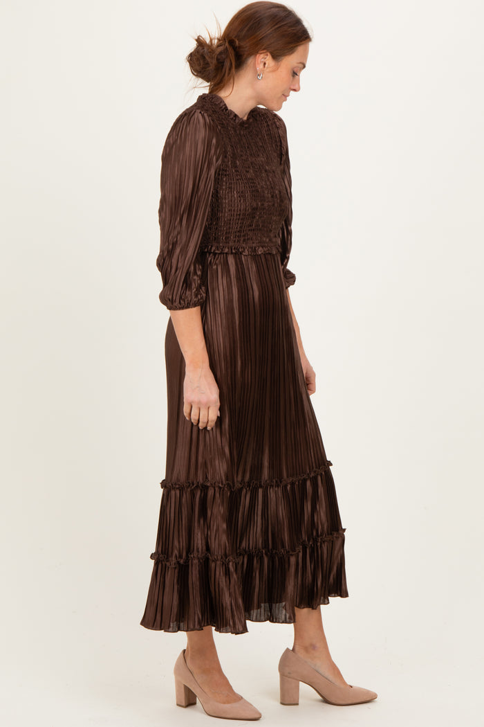 woman wearing a brown pleated midi dress with ruffled tiers and long sleeves, paired with light beige heels