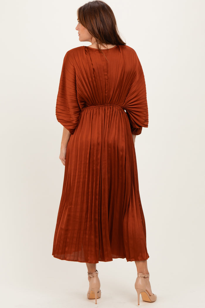 woman wearing a rust-colored pleated midi dress with a cinched waist and balloon sleeves, showing the back view