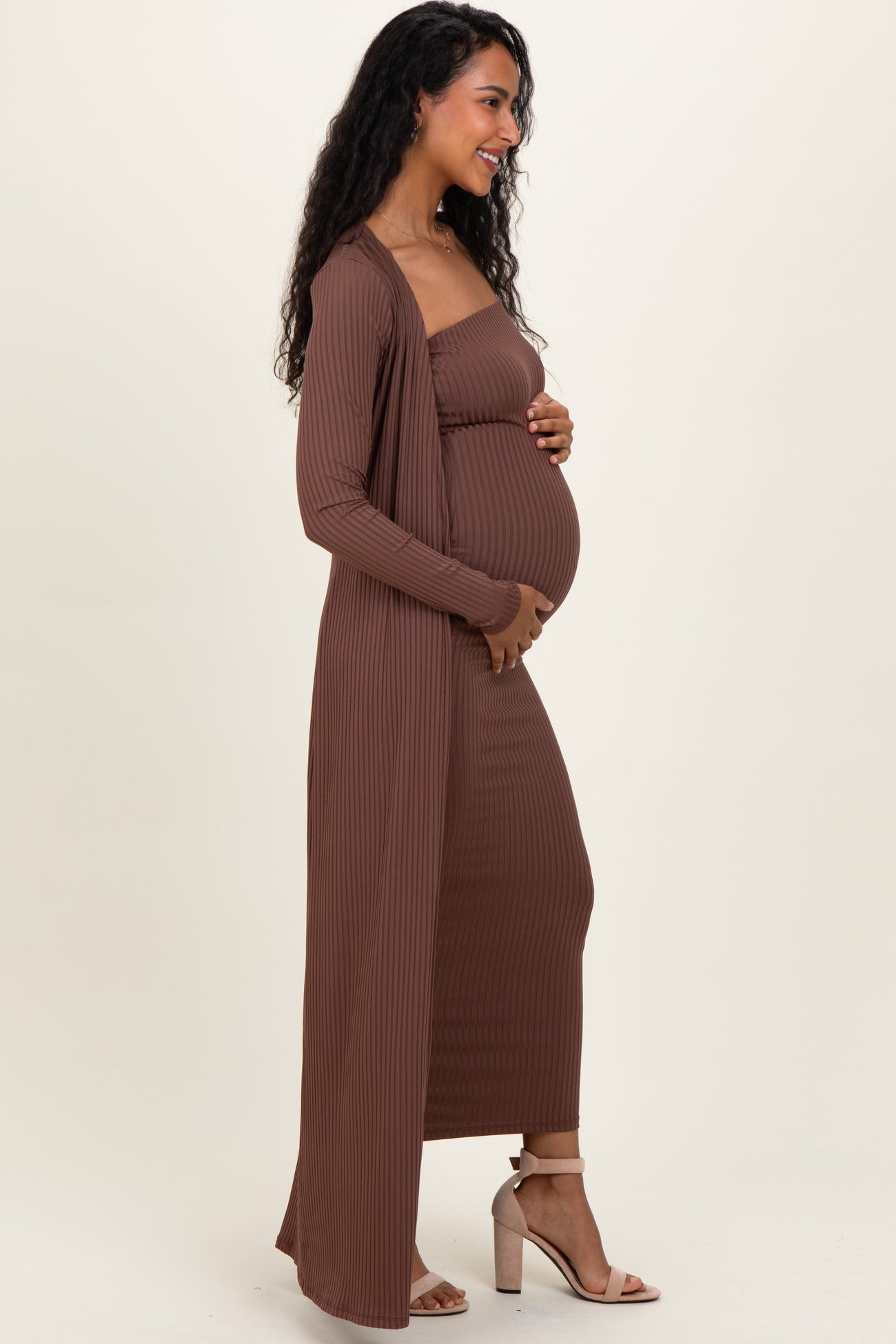 woman wearing a brown maternity ribbed dress with a long cardigan and holding her baby bump