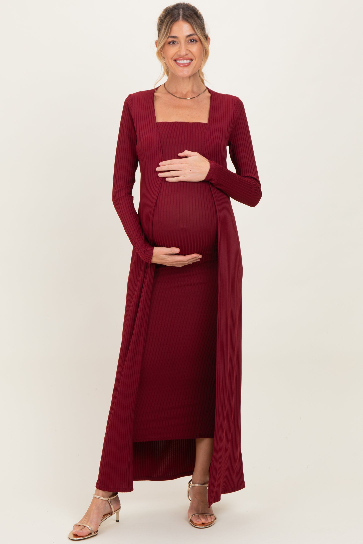 woman wearing a burgundy ribbed maternity dress with a square neckline and long sleeves, holding her baby bump