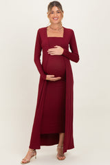 woman wearing a burgundy ribbed maternity dress with a square neckline and long sleeves, holding her baby bump