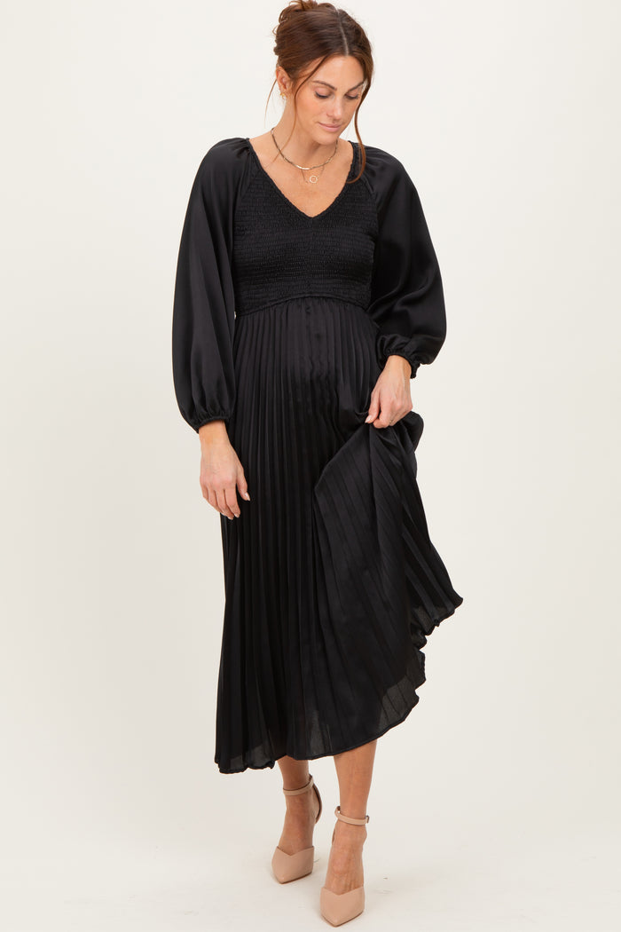 woman wearing a black pleated midi dress with a smocked bodice and long puff sleeves
