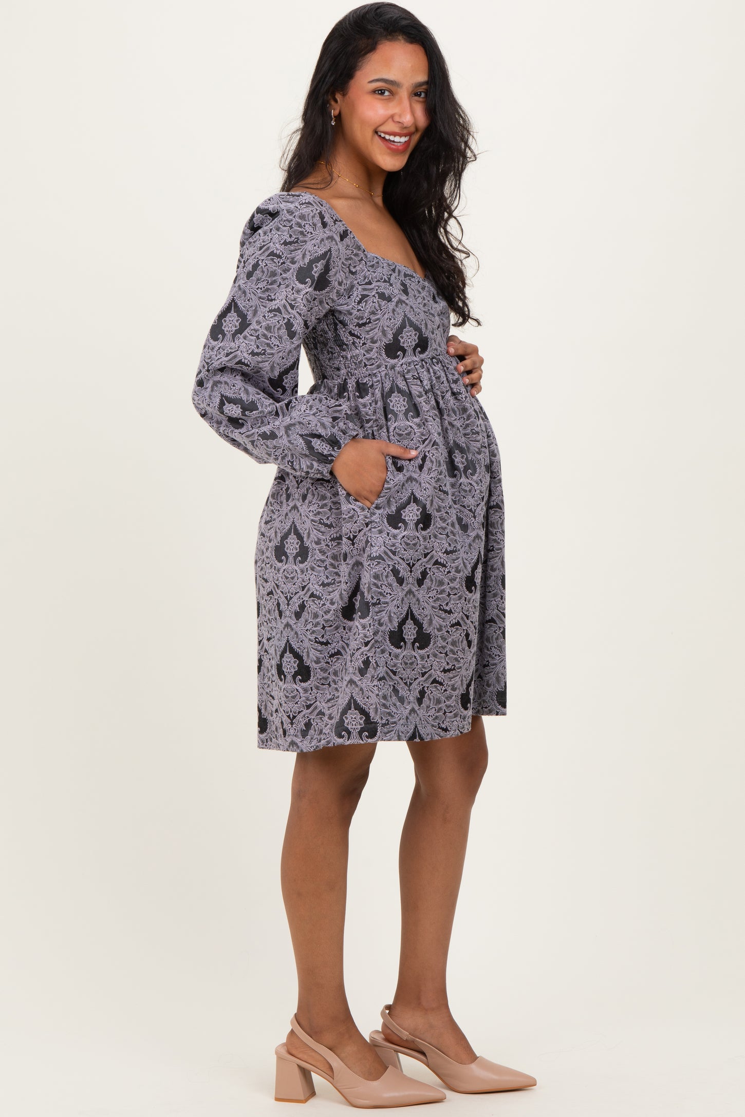 woman wearing a gray patterned maternity dress with long sleeves and pockets, showcasing her baby bump