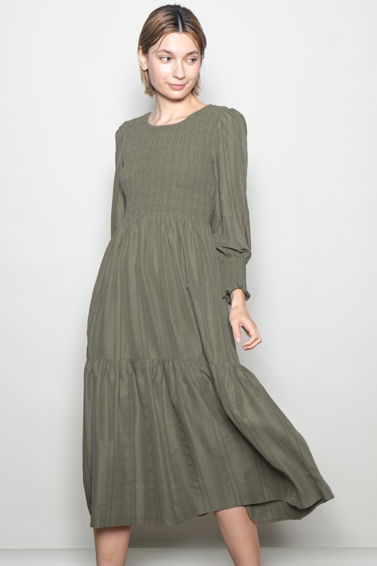 woman wearing an olive green long sleeve smocked midi dress with tiered skirt