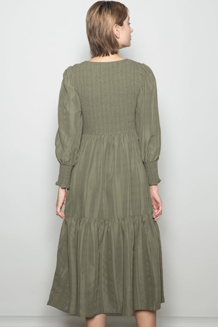woman wearing an olive green smocked back midi dress with long puff sleeves and a tiered skirt