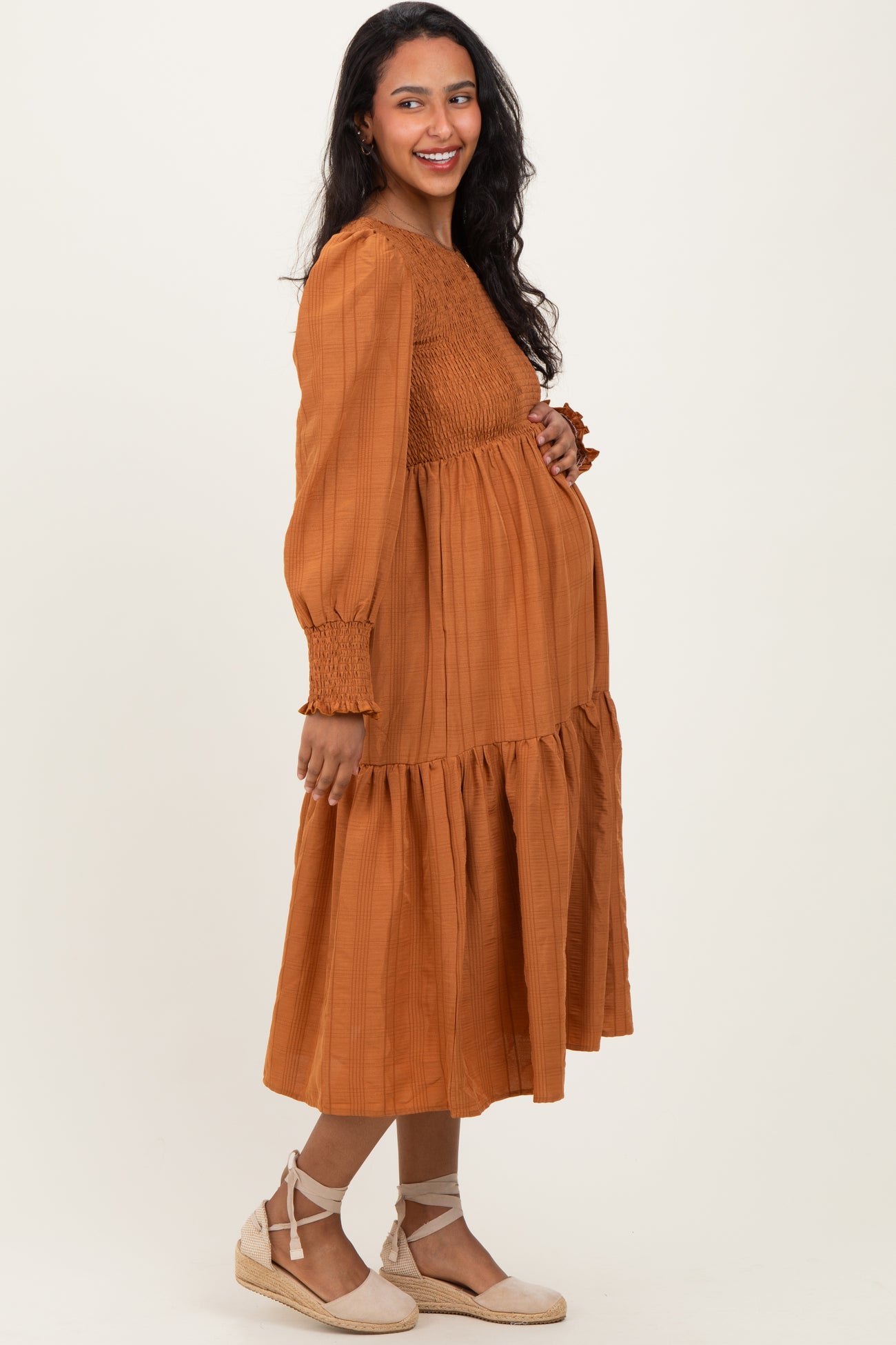 woman wearing a rust-colored maternity dress with a smocked bodice and tiered skirt, showcasing her baby bump