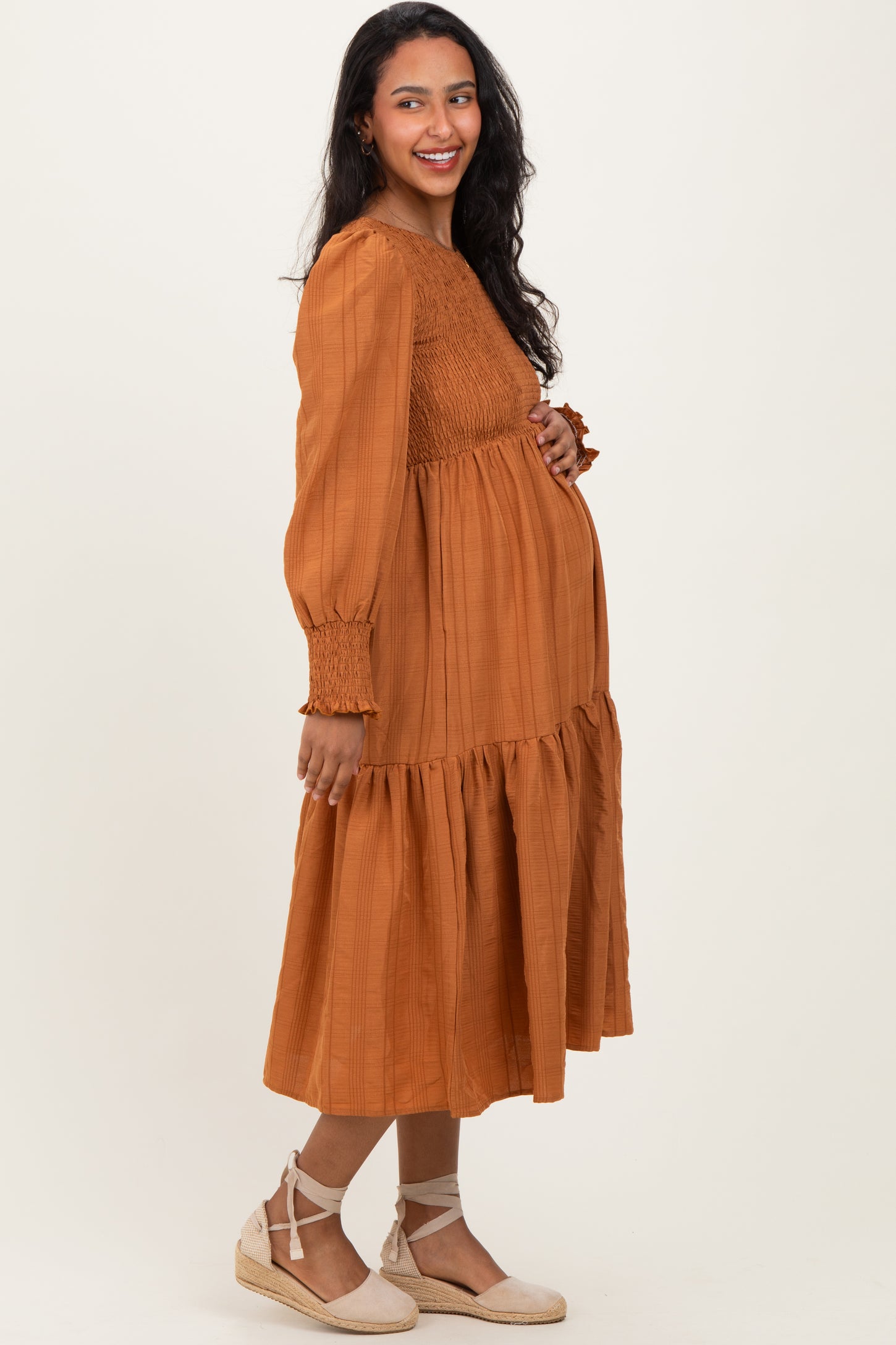 woman wearing a rust-colored maternity dress with a smocked bodice and tiered skirt, showcasing her baby bump