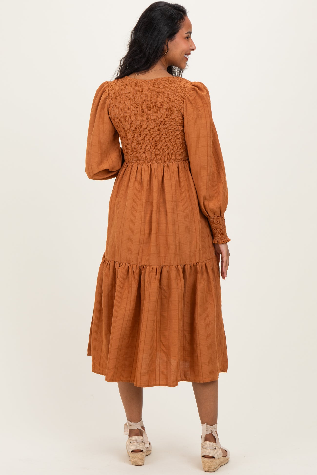 woman wearing a rust colored maternity dress with a smocked bodice and tiered skirt, showing her back view