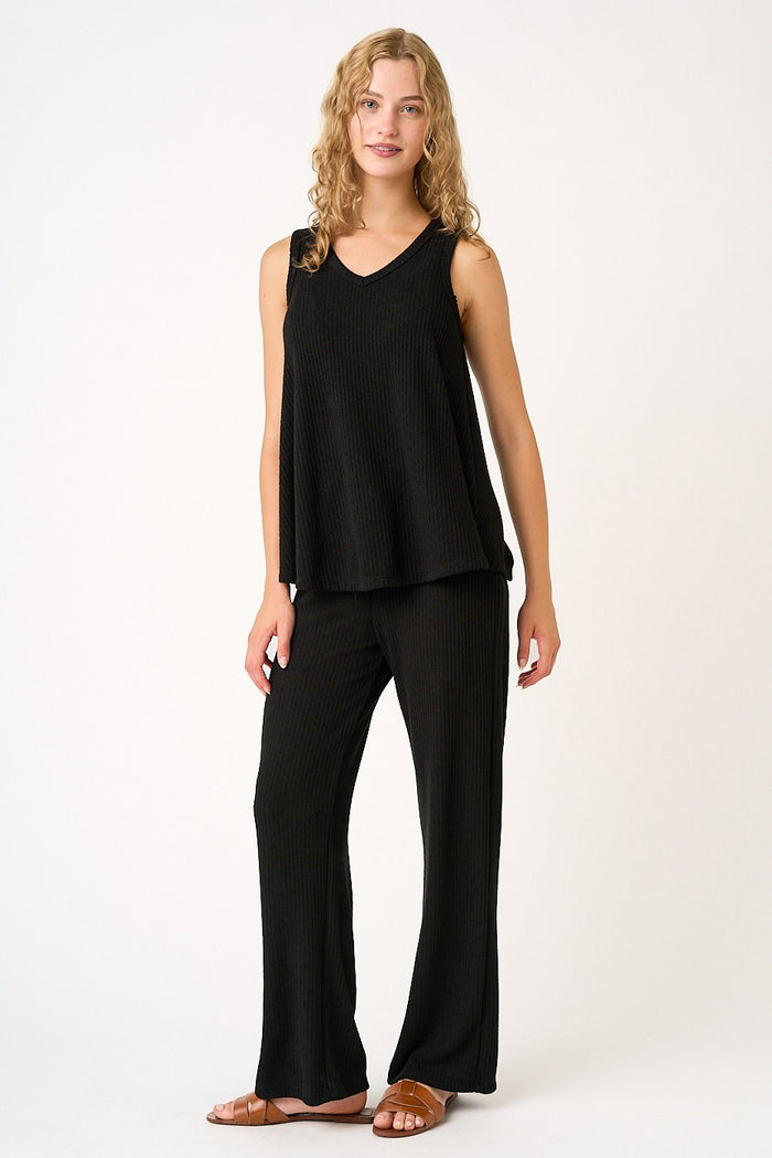 woman wearing a black ribbed sleeveless top and matching wide-leg pants, standing with a relaxed pose