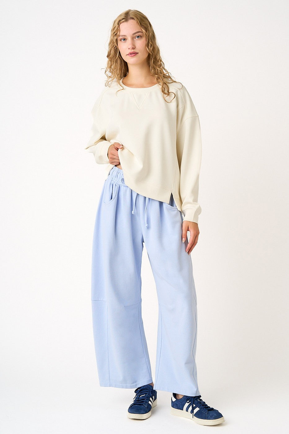 woman wearing a beige oversized sweatshirt and light blue wide-leg pants with navy blue sneakers