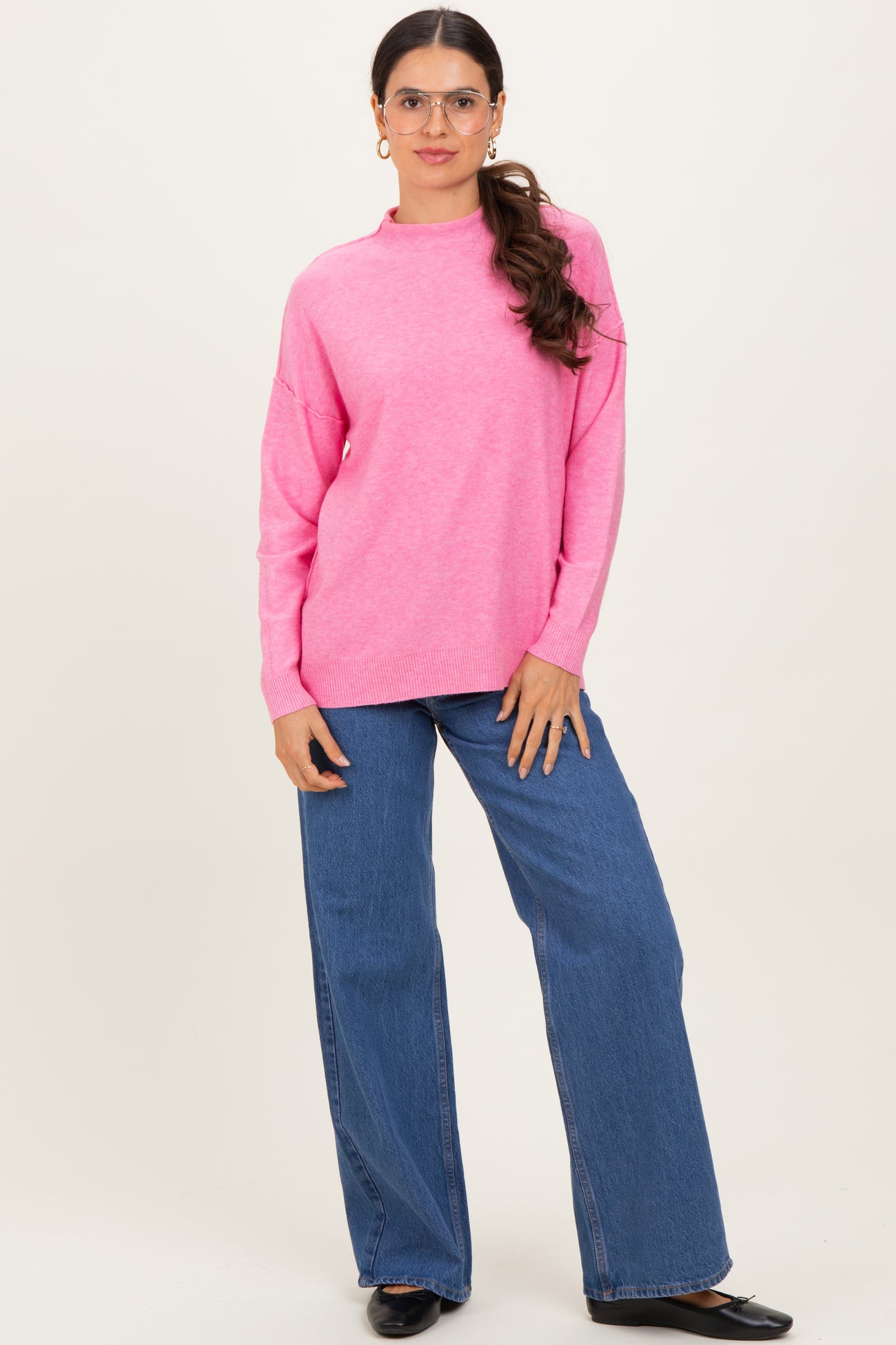 woman wearing a bright pink oversized knit sweater and blue wide-leg jeans, standing with hands on hips