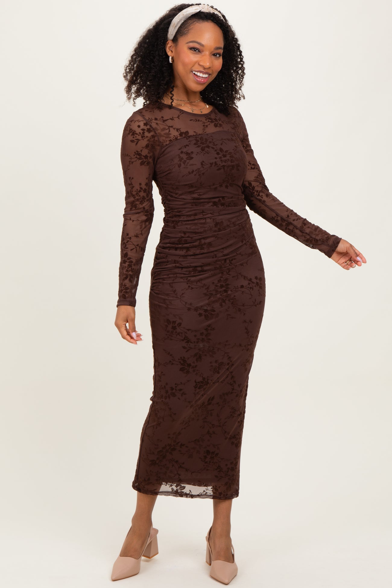 woman wearing a brown long sleeve ruched midi dress with floral lace details and styled with a headband