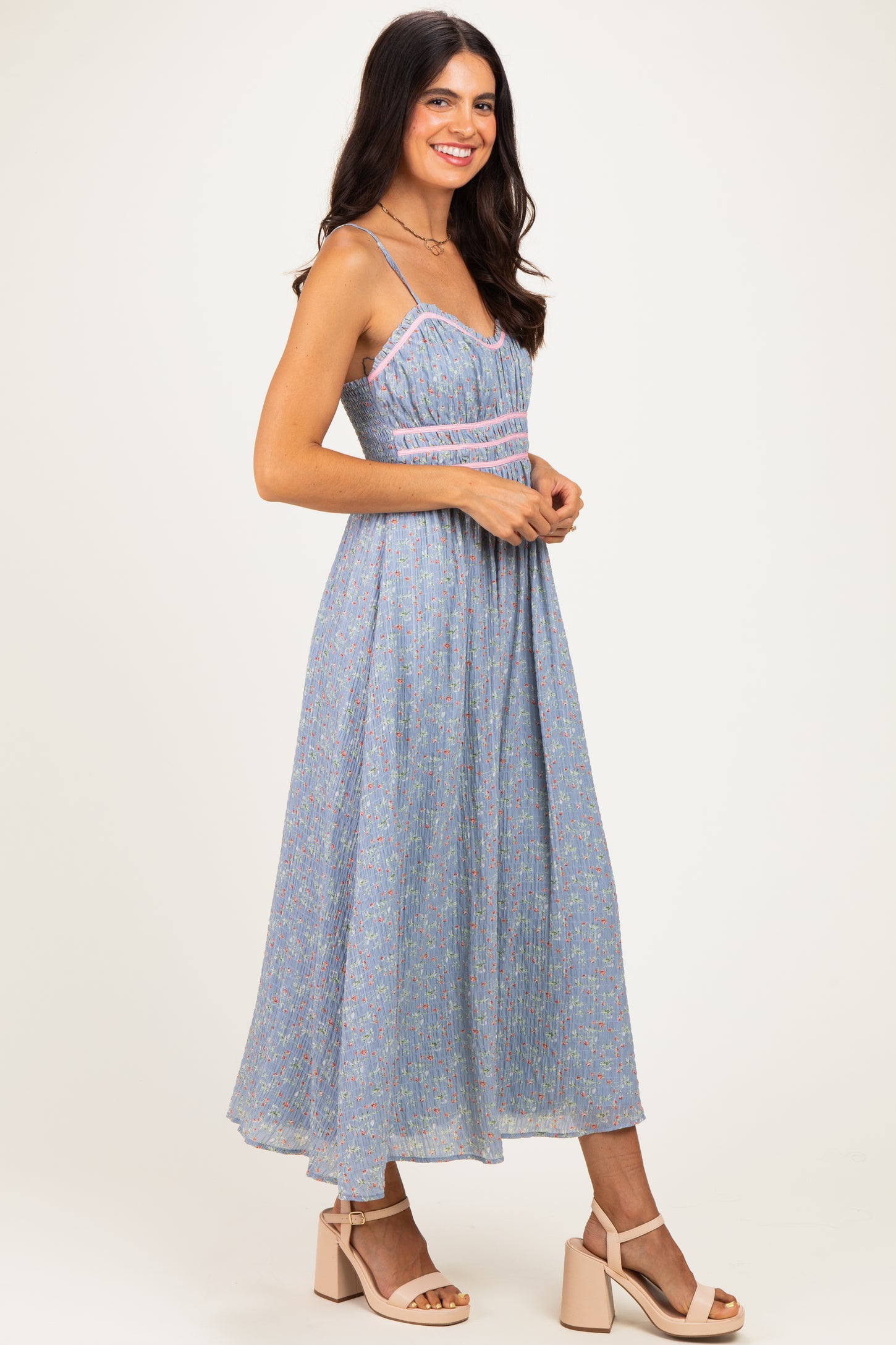 woman wearing a blue floral midi dress with spaghetti straps and a fitted bodice, paired with blush heels