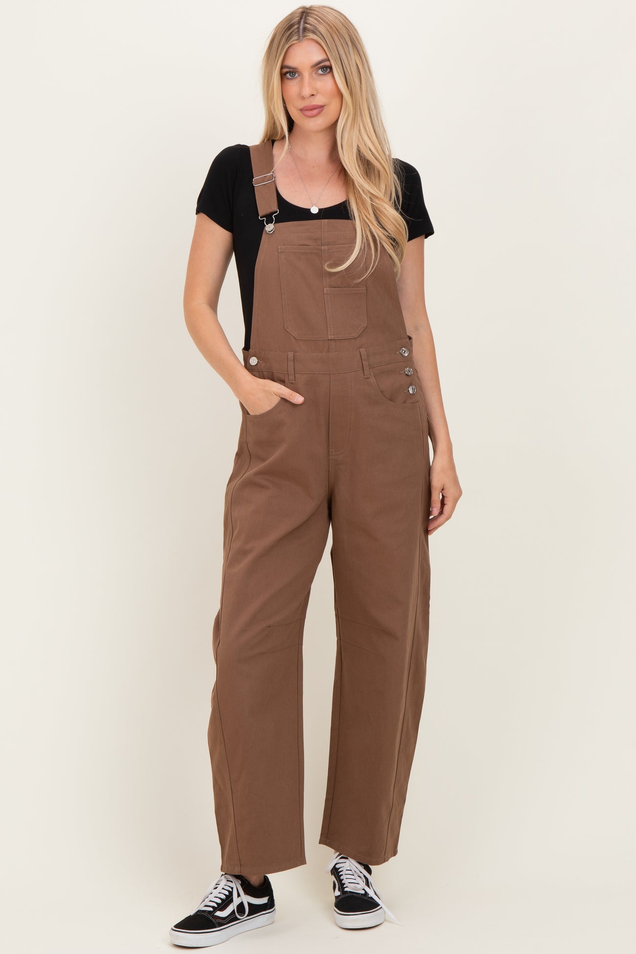 woman wearing a black t-shirt and brown overalls with wide legs and side buttons