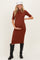 woman wearing a rust ribbed maternity midi dress and holding her baby bump, paired with black knee-high boots and a white hat
