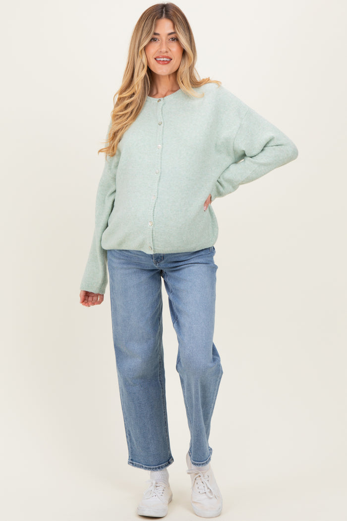 woman wearing a mint green maternity cardigan and light blue jeans, showing her baby bump