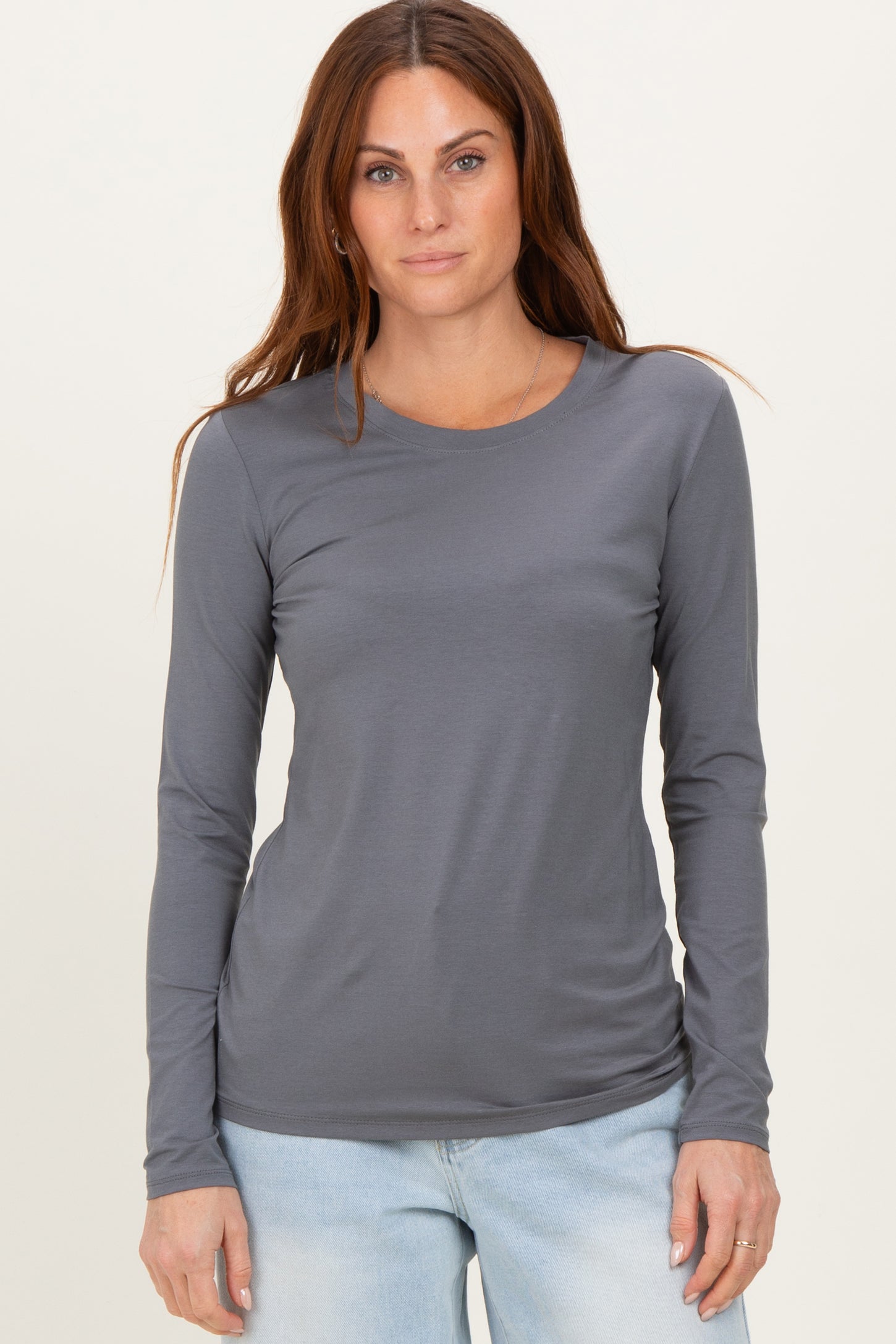 woman wearing a gray long sleeve top with a round neckline and fitted style, posed against a neutral background