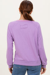 woman wearing a lavender long sleeve sweatshirt with a relaxed fit and back logo detail, styled with jeans