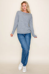 woman wearing a light gray long sleeve sweater paired with blue jeans and white sneakers standing against a neutral background