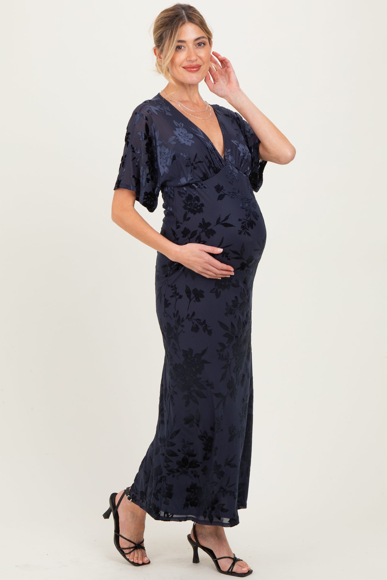 woman wearing a navy floral maxi maternity dress with a deep v-neck and holding her baby bump