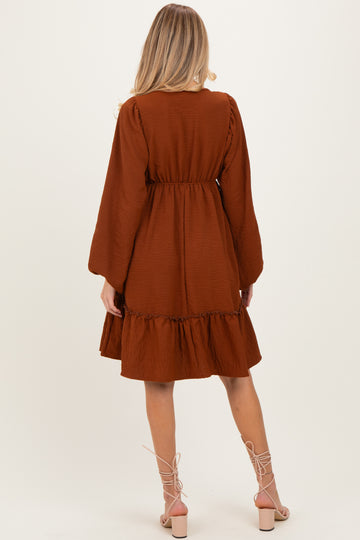 woman wearing a brown maternity dress with long sleeves and a ruffled hem, showing her back