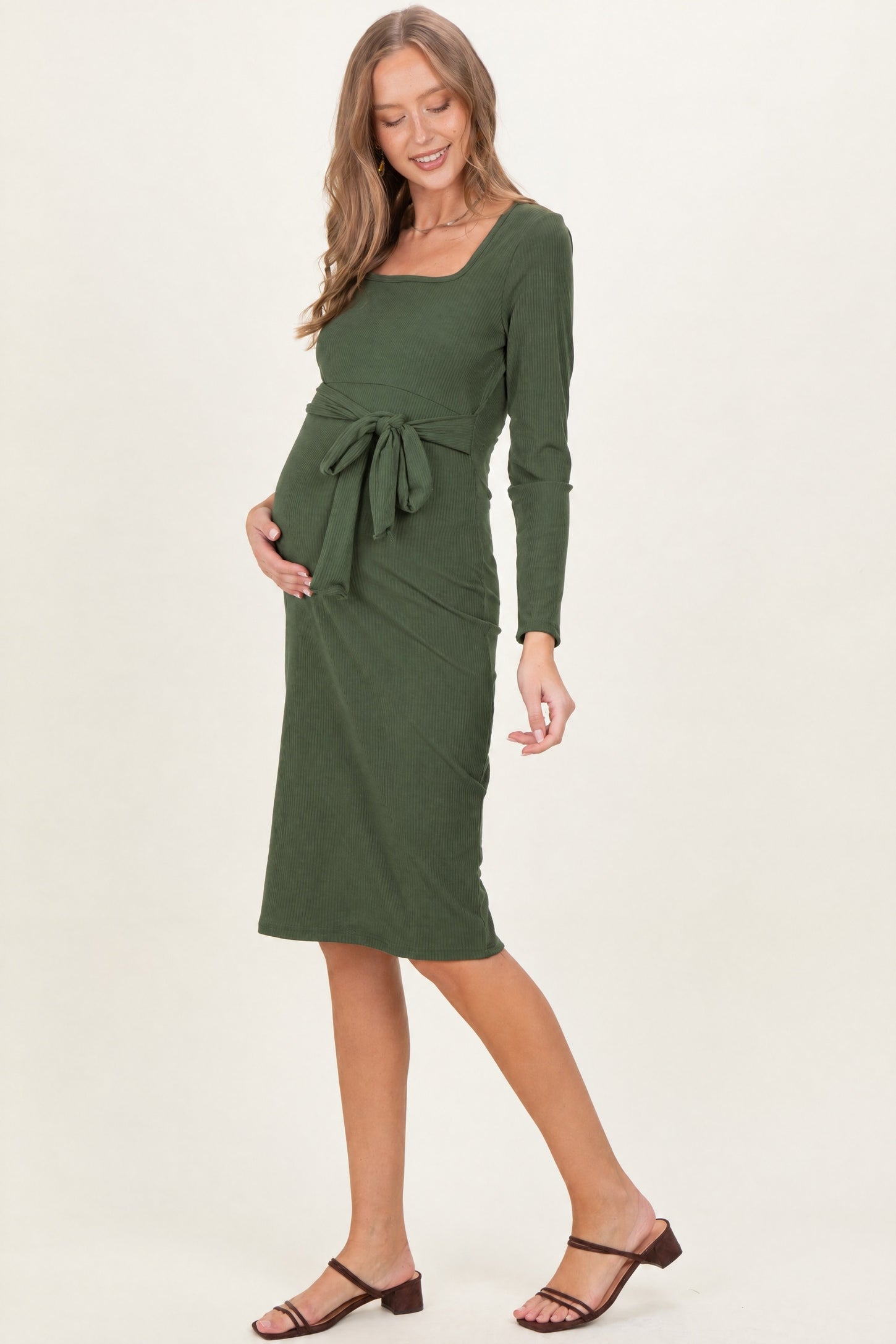 woman wearing a green long sleeve maternity dress with a square neckline and tie waist, showing her baby bump