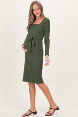 woman wearing a green long sleeve maternity dress with a square neckline and tie waist, showing her baby bump