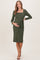 woman wearing a dark green ribbed maternity dress with a square neckline and tied waist, cradling her baby bump