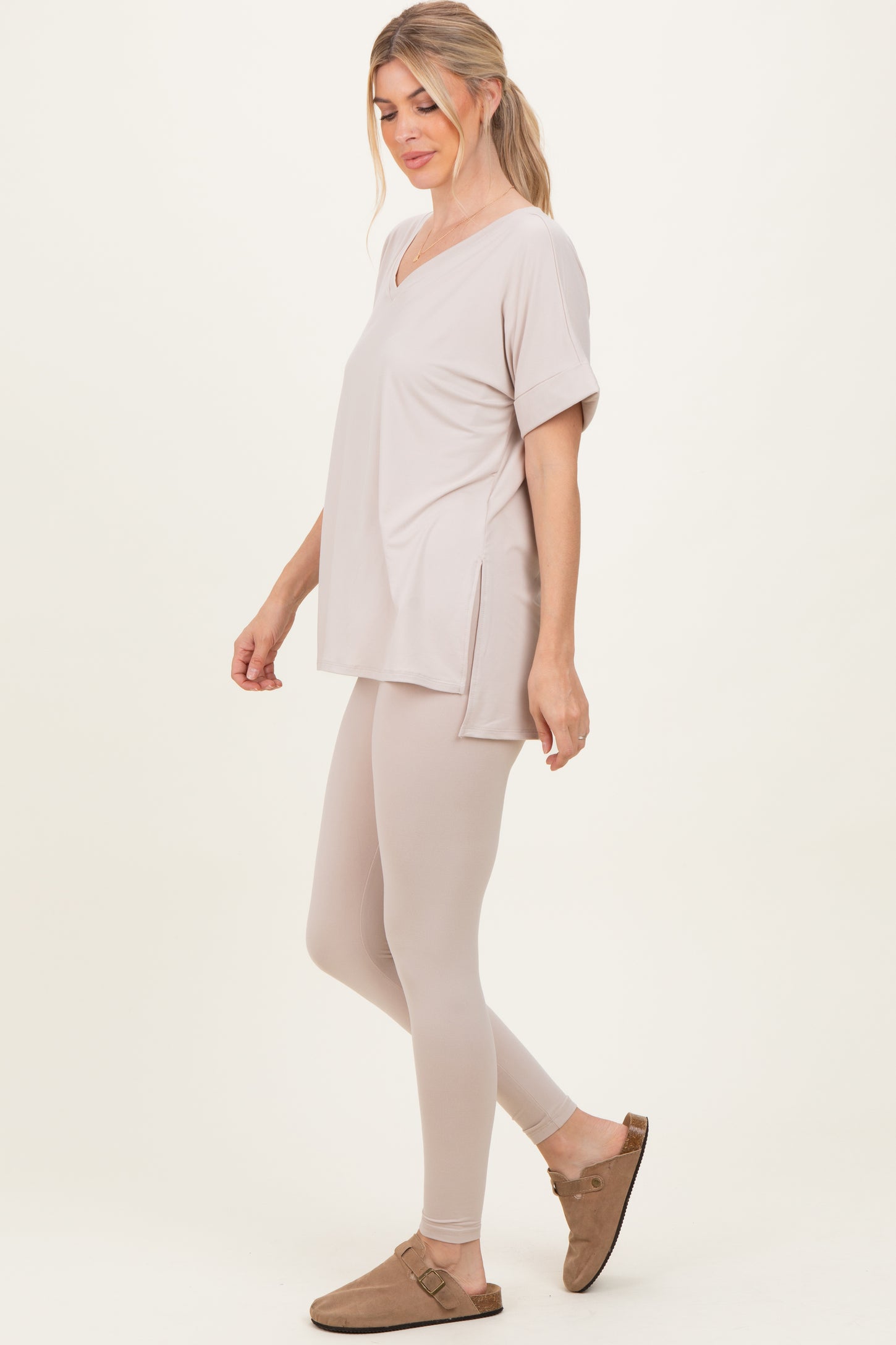 woman wearing a light beige oversized v-neck top with side slits and matching beige leggings, styled with brown slip-on shoes