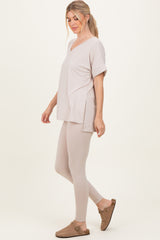 woman wearing a light beige oversized v-neck top with side slits and matching beige leggings, styled with brown slip-on shoes