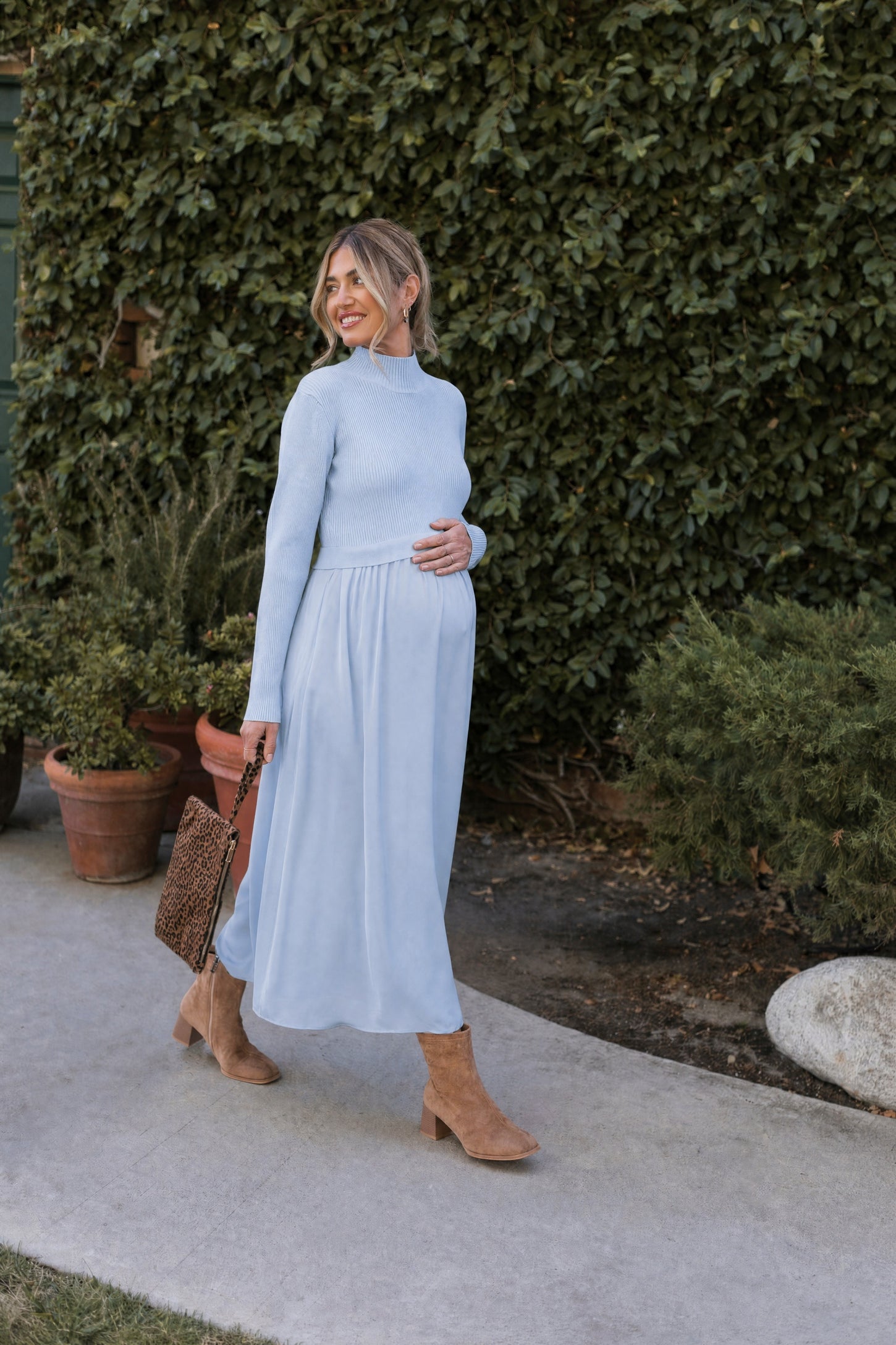 woman wearing a light blue maternity knit sweater and a flowy light blue maternity maxi skirt, holding her baby bump
