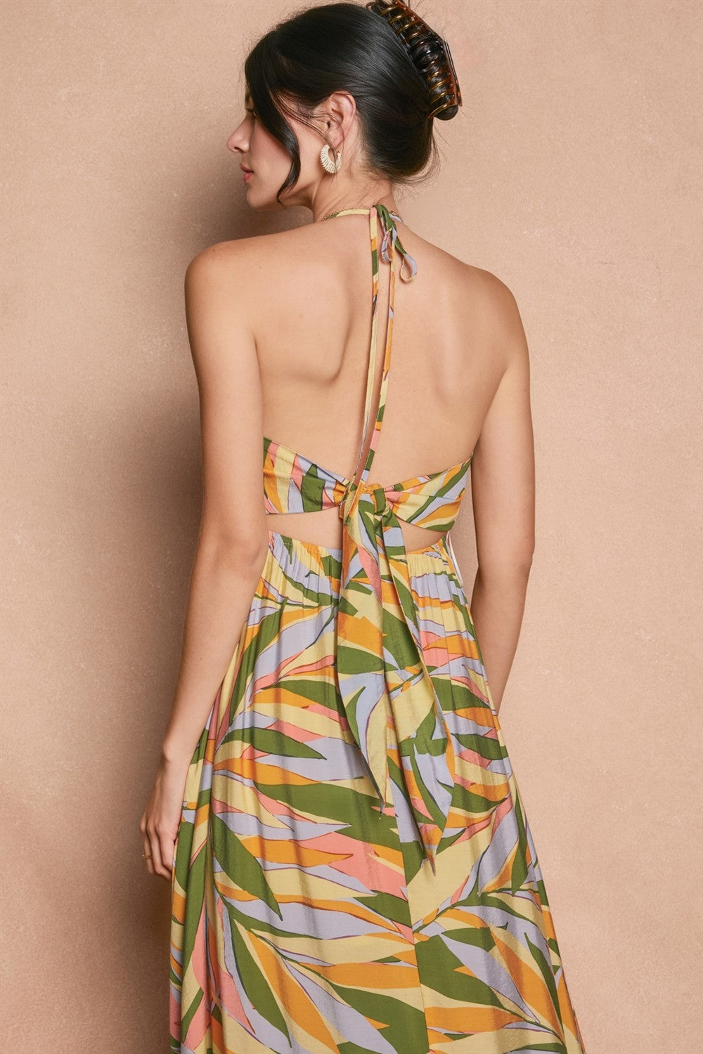woman wearing a multicolor halter dress with a tied back and tropical leaf print, view from the back