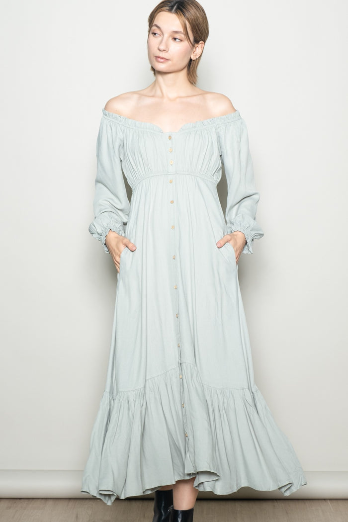 woman wearing a light green off-the-shoulder maxi dress with button details and pockets