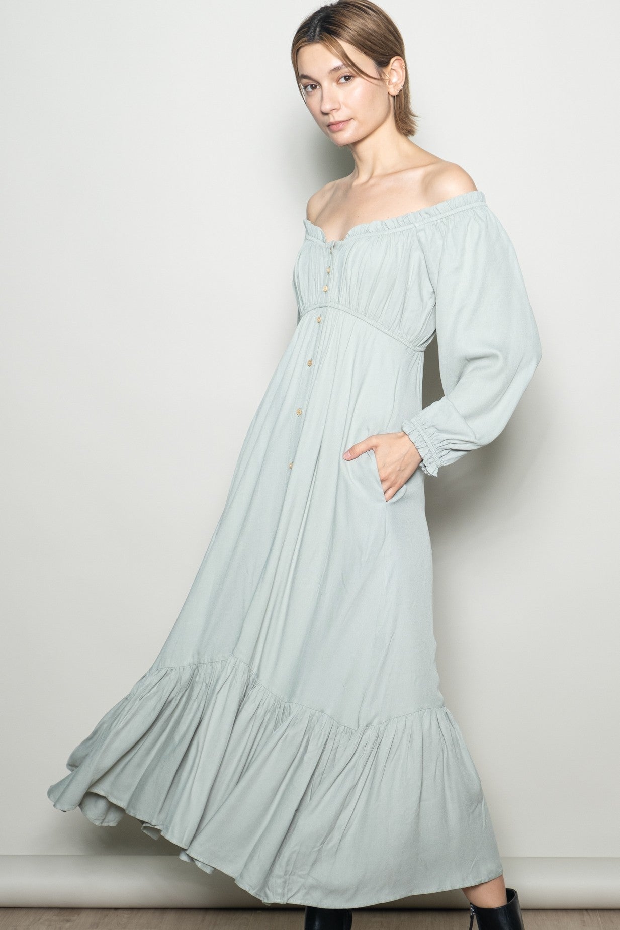woman wearing a light green off-the-shoulder maxi dress with puff sleeves and side pockets, featuring a tiered skirt