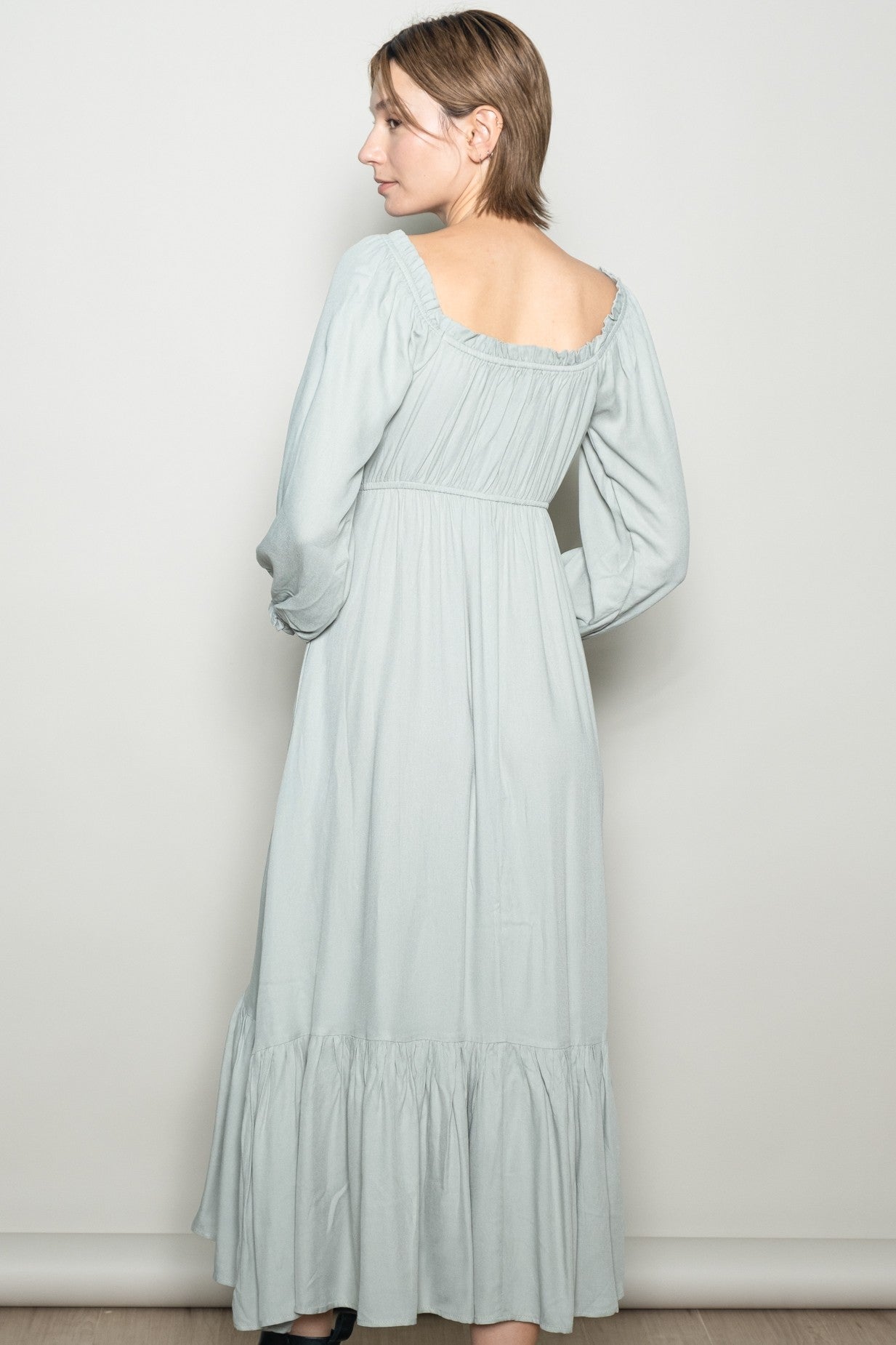 woman wearing a light green long sleeve maxi dress with a ruffled hem and an open back design