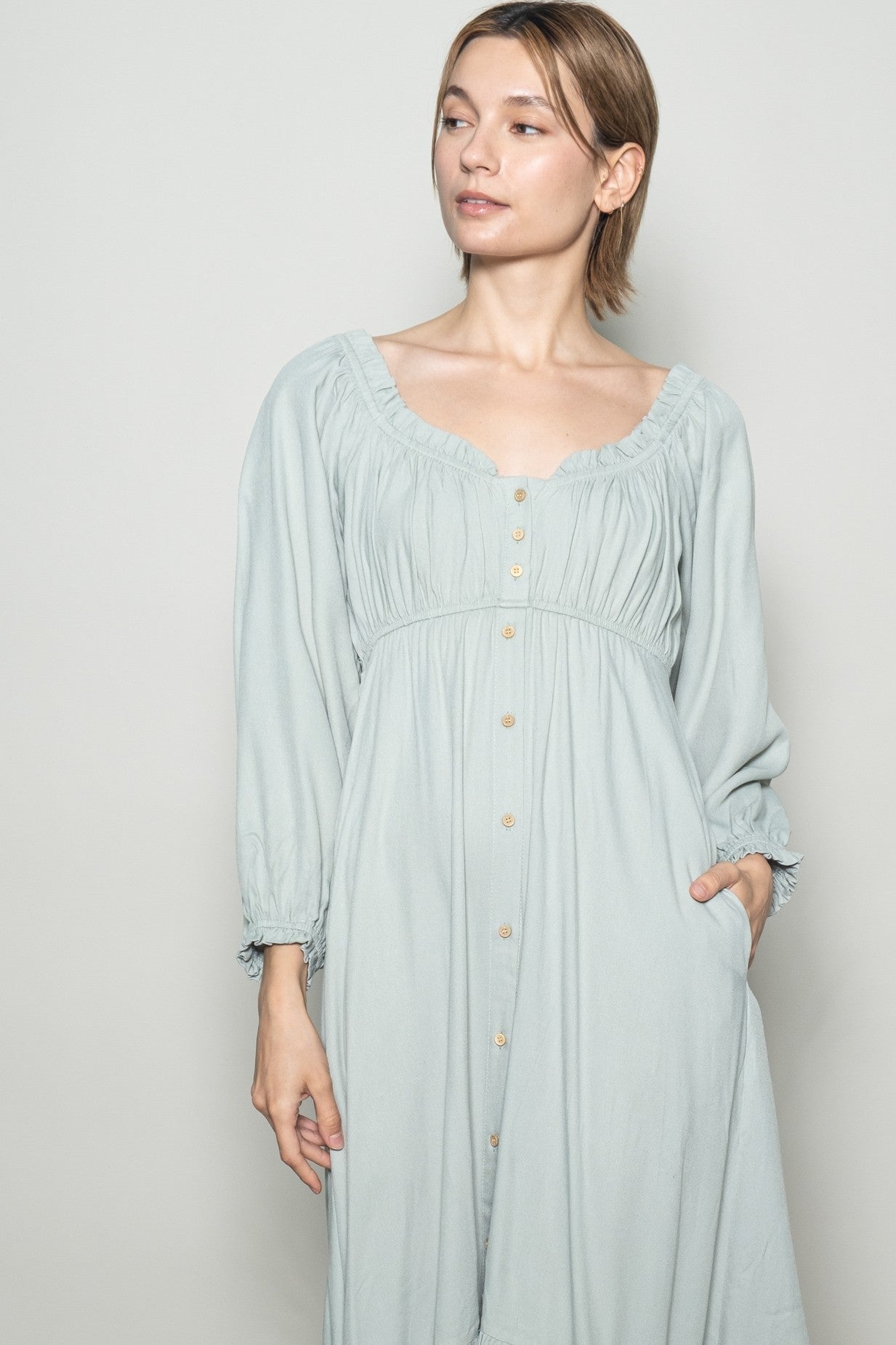 woman wearing a light blue long sleeve button-down dress with a square neckline and gathered details