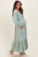 woman wearing a light green long sleeve maternity dress with a tiered skirt and a visible baby bump
