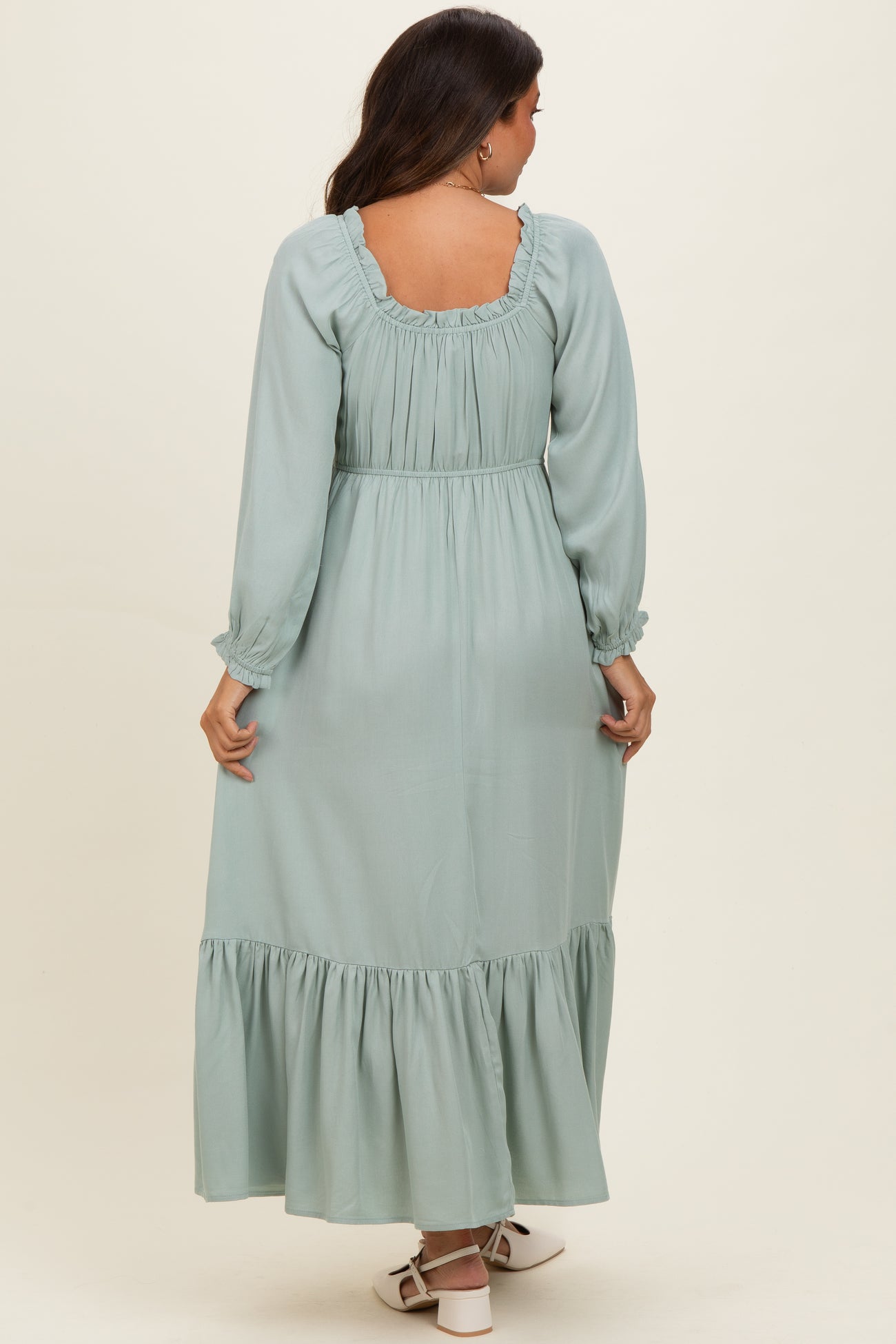 woman wearing a mint green long sleeve maternity maxi dress with ruffled details and a fitted waist