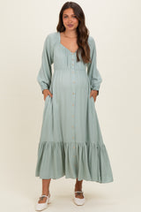 woman wearing a light green maternity maxi dress with button details and pockets, featuring a ruffled hem and long sleeves, showing her baby bump