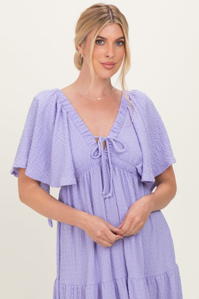 woman wearing a lavender puff sleeve dress with a tie neckline and a tiered skirt