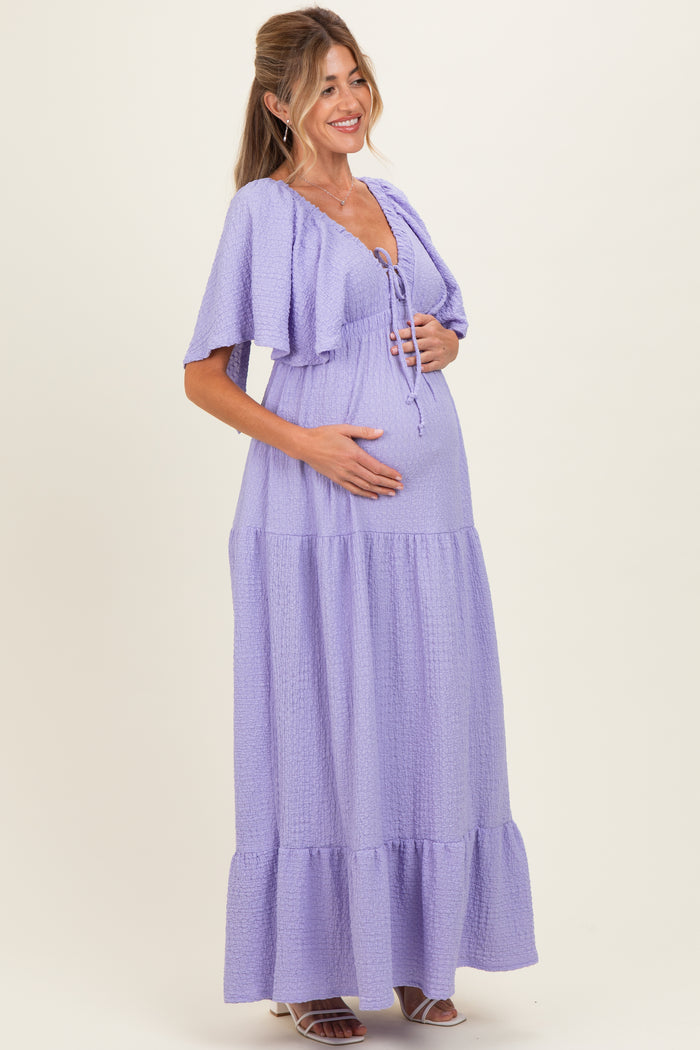 woman wearing a lavender maternity maxi dress with short sleeves and a tie-front detail, holding her baby bump