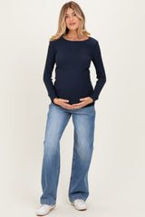 woman wearing a navy ribbed long sleeve maternity top and holding her baby bump, paired with light blue wide-leg jeans