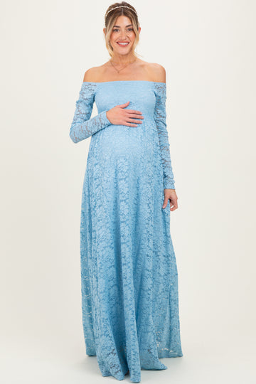 woman wearing a light blue off-the-shoulder lace maternity gown with long sleeves and cradling her baby bump