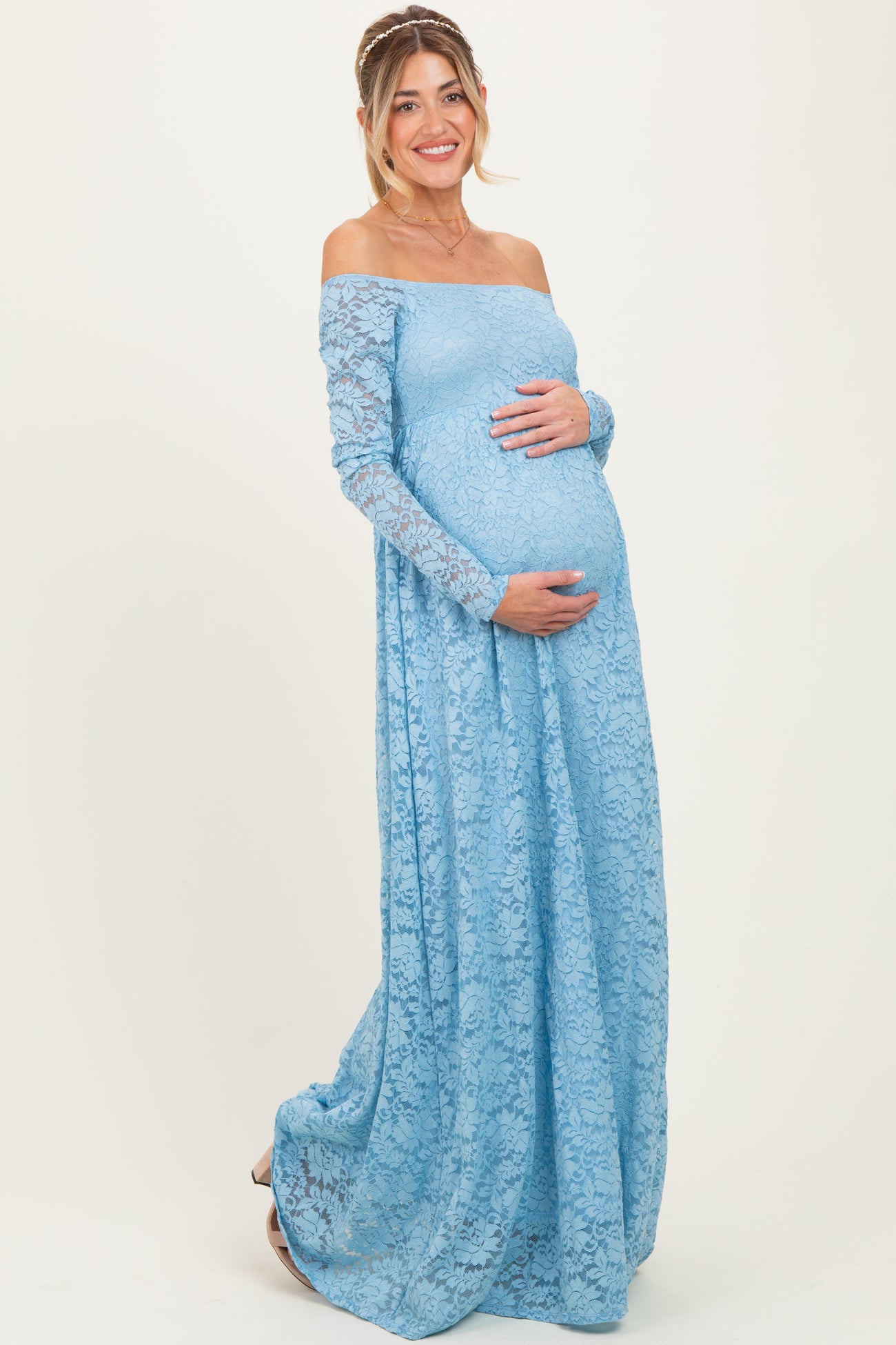 woman wearing a light blue off-shoulder lace maternity gown and holding her baby bump