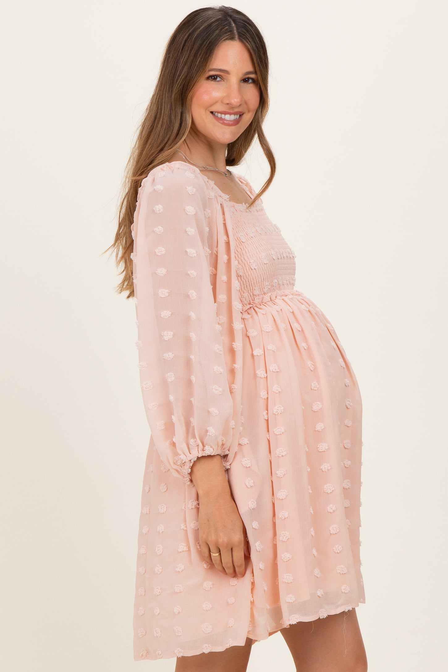 woman wearing a blush pink maternity dress with balloon sleeves and a smocked bodice, showing her baby bump