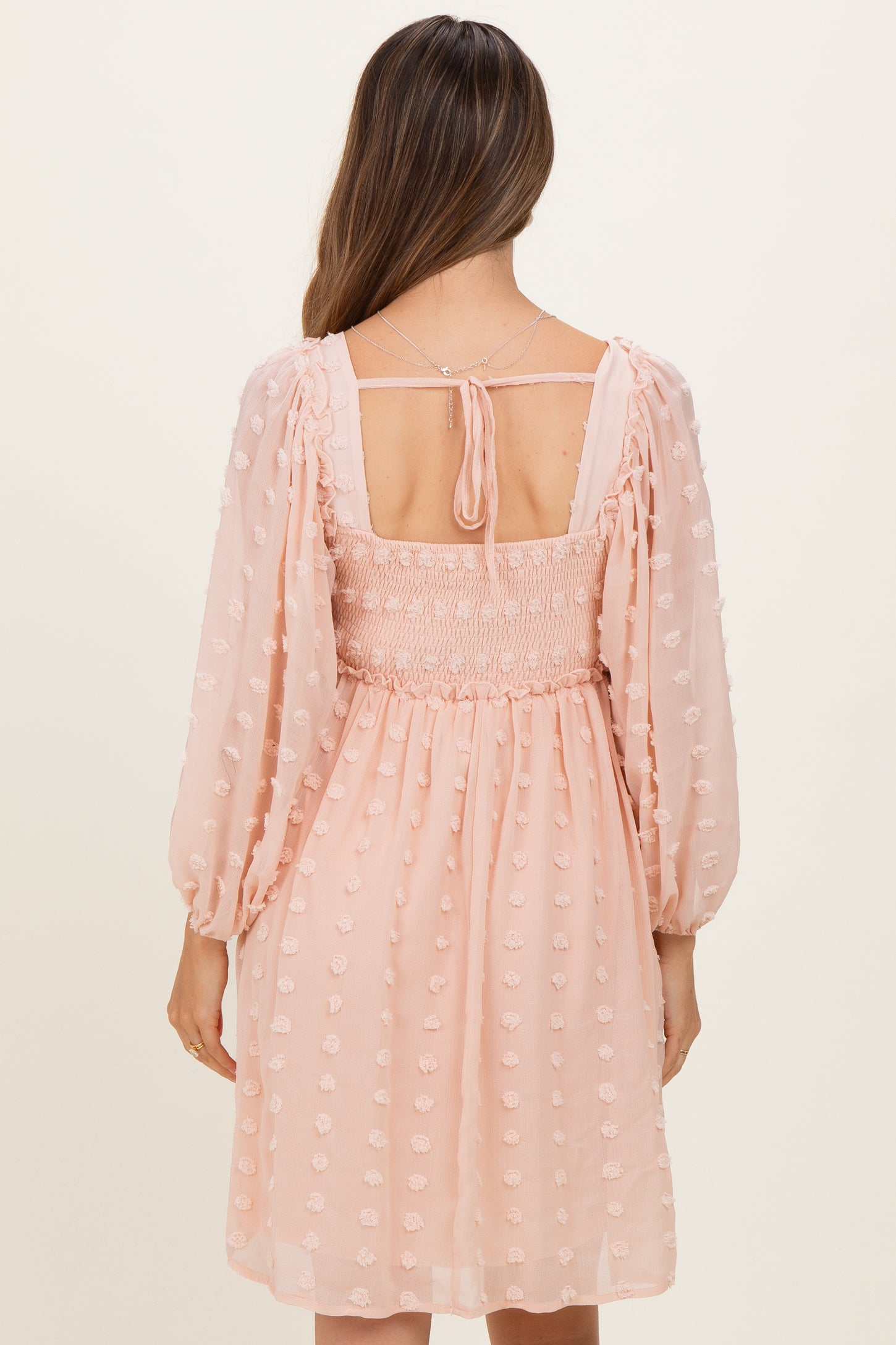 woman wearing a blush pink maternity dress with smocked bodice and puff sleeves, seen from the back