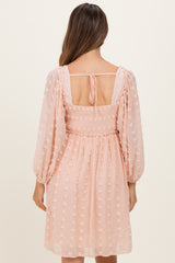 woman wearing a blush pink maternity dress with smocked bodice and puff sleeves, seen from the back